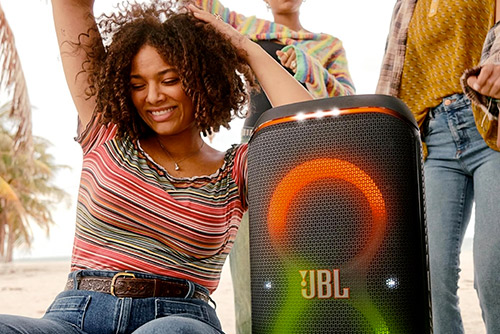Jeune femme dansant près d'une enceinte Bluetooth JBL PartyBox Club 120 lumineuse.