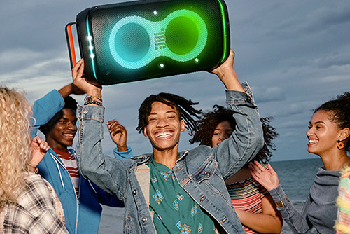 Enceinte Bluetooth JBL PartyBox Club 120 levée en l'air lors d'une fête sur la plage