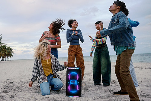 Groupe d'amis dansant sur la plage avec enceinte Bluetooth JBL PartyBox Club 120