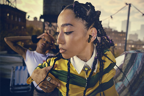 Femme portant écouteurs JBL Wave Buds noirs en extérieur, écoute sans fil urbaine