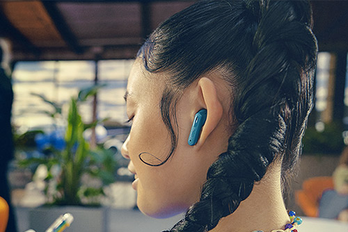 Jeune femme avec écouteurs JBL Wave Buds bleus, utilisation confortable en intérieur