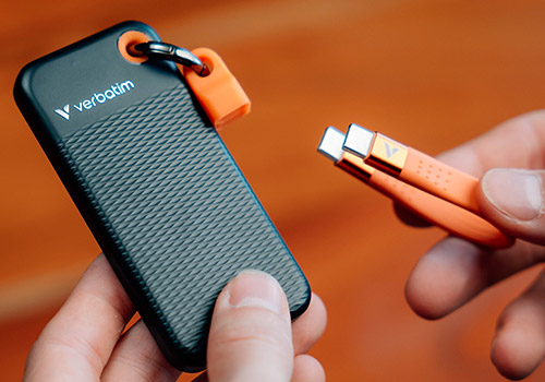 SSD Verbatim portable noir posé sur une surface en bois, avec dragonne orange attachée au coin