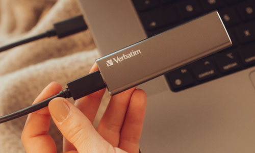 Main tenant un SSD Verbatim Vx500 branché à un ordinateur via câble USB-C