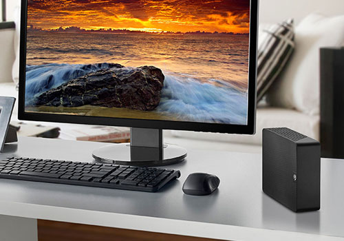Disque dur Seagate One Touch placé sur un bureau moderne à côté d'un écran affichant un paysage en mer