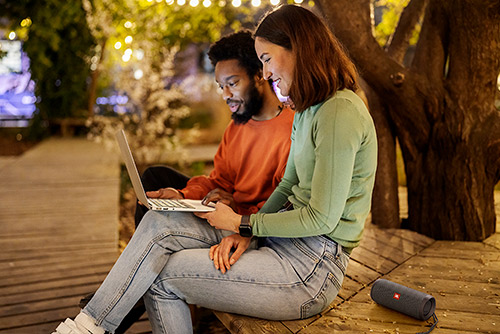 nceinte Bluetooth JBL Flip Essential 2 utilisée en extérieur de nuit près d'un couple sur ordinateur