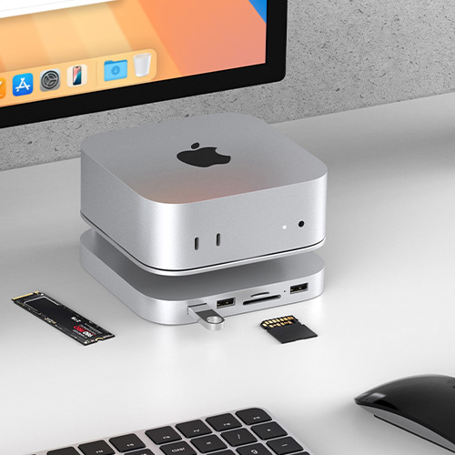 Station d'accueil en aluminium positionnée sous un Mac Studio, équipée de multiples ports et d'un emplacement pour SSD M.2, sur un bureau moderne avec clavier Apple.