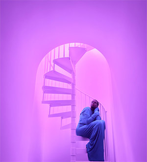 Photo artistique prise avec l'iPhone 17 Pro montrant une femme assise au bas d'un escalier en colimaçon éclairé en violet