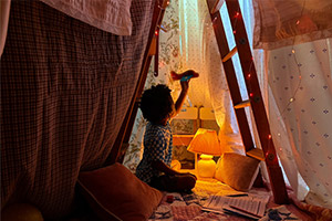 Photo en basse luminosité d'un enfant jouant avec une lampe dans une cabane improvisée, capturée avec l'iPhone 17