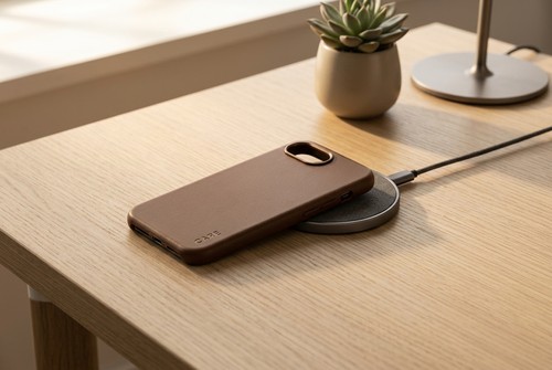 Coque PanzerGlass CARE Solo Brown posee sur un chargeur sans fil MagSafe sur un bureau en bois